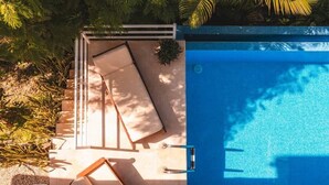 A swimming pool with a sun lounger and a small table, surrounded by greenery. - Great location, walking distance to the beach -E (Puntarenas)