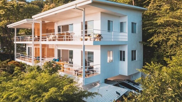 A modern two-story house with a balcony, surrounded by lush greenery. - Great location, walking distance to the beach -E (Puntarenas)