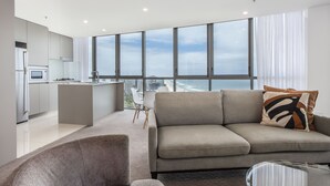 A modern living room with a sofa, a glass coffee table, and a view of the city through large windows.