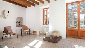 Una habitación amplia con techo de madera, un ventanal grande y una puerta. Hay varias sillas y una mesa con una escultura.