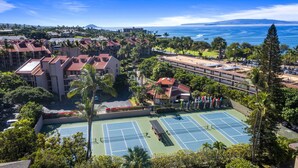 Un complexe hôtelier comprenant plusieurs bâtiments, un court de tennis et offrant une vue sur l’océan.