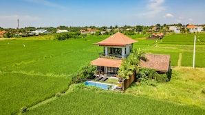 Una casa con piscina rodeada de exuberantes campos verdes y un cielo azul despejado.