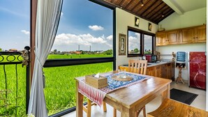 Un comedor con vistas a un campo verde, una mesa de madera con un mantel individual, y una cocina con armarios de madera y un refrigerador rojo.