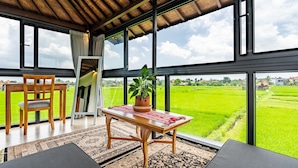 Una habitación con un ventanal grande, una mesa de madera, una silla y una planta en maceta.