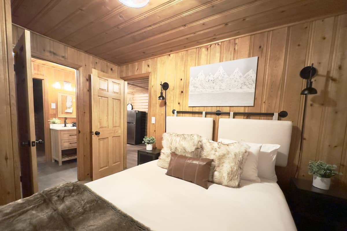 Un dormitorio con un panel de madera en la pared, una cama con ropa de cama blanca, un plaid suave y un cuadro sobre la cama.