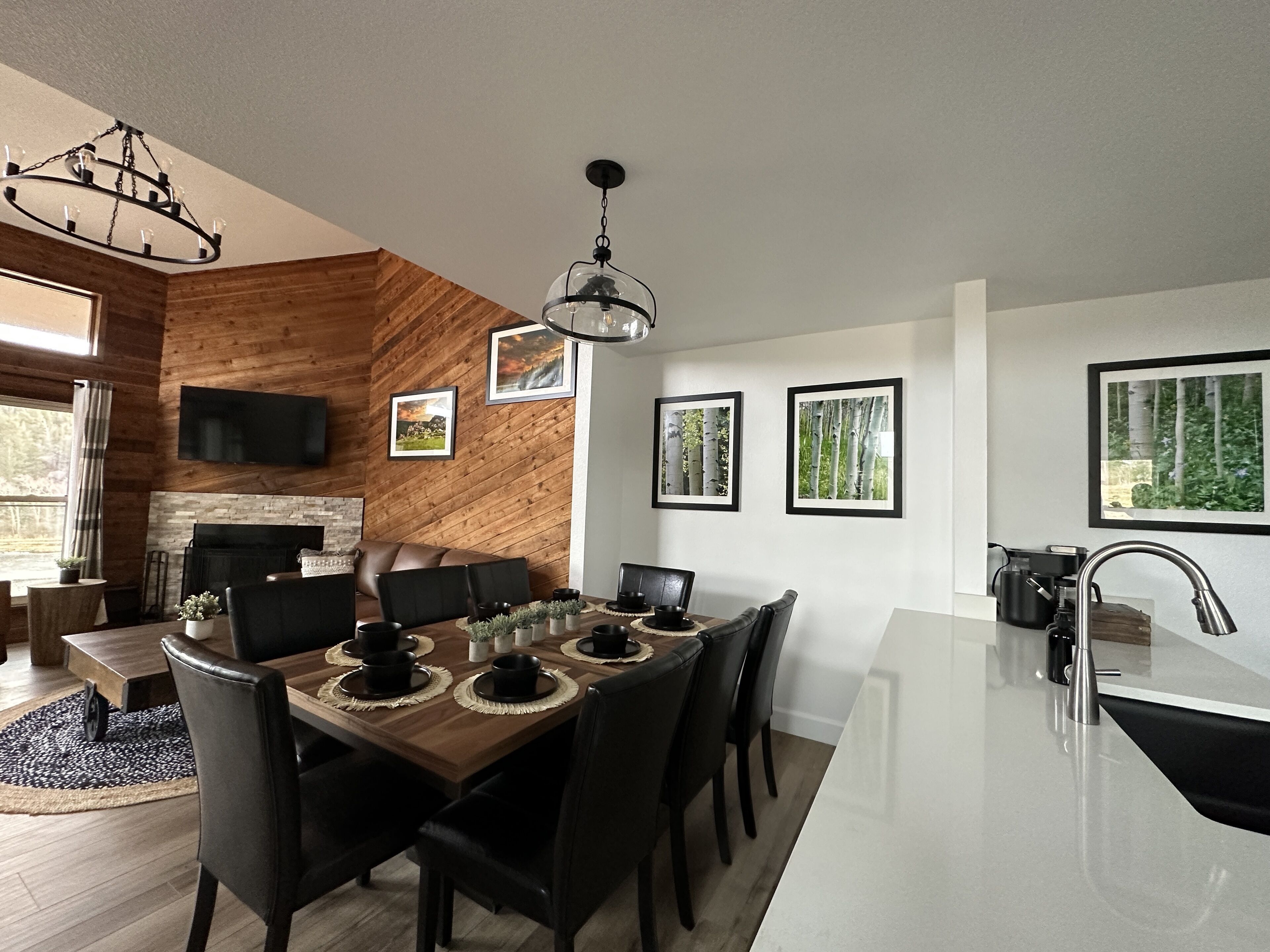 A modern kitchen with a central island, a dining area with a wooden table and chairs, and a living area with a fireplace and leather sofa.