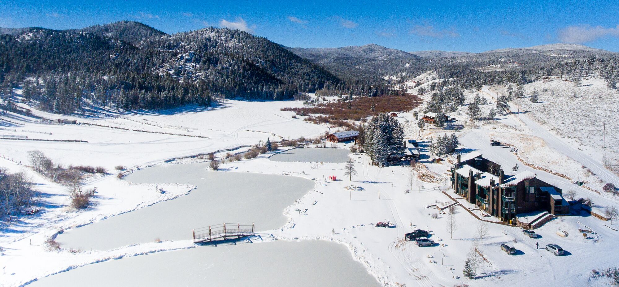 A mountainous area with snow-covered fields, a lake, and buildings.