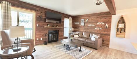 Ein gemütliches Wohnzimmer mit Kamin, Holzwänden, einer Couch, einem Couchtisch und einem Fernseher über dem Kamin.
