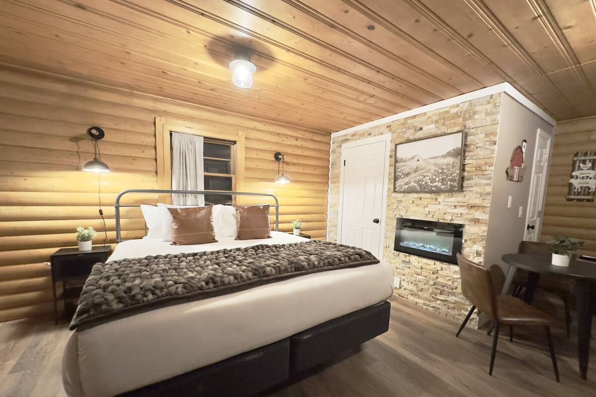 Un dormitorio rústico de madera con cama, lámparas de noche, una chimenea de piedra y un comedor.
