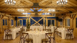A large, rustic wooden hall with multiple round tables set for dining, each with white tablecloths and wooden chairs. - Beaver Meadows Resort Ranch (Red Feather Lakes)