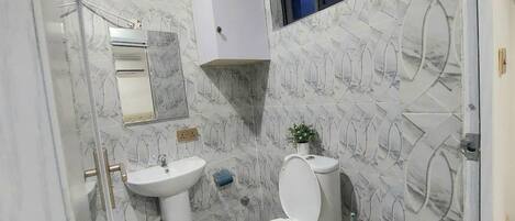 Baño con lavamanos pedestal, inodoro y pequeña ventana.