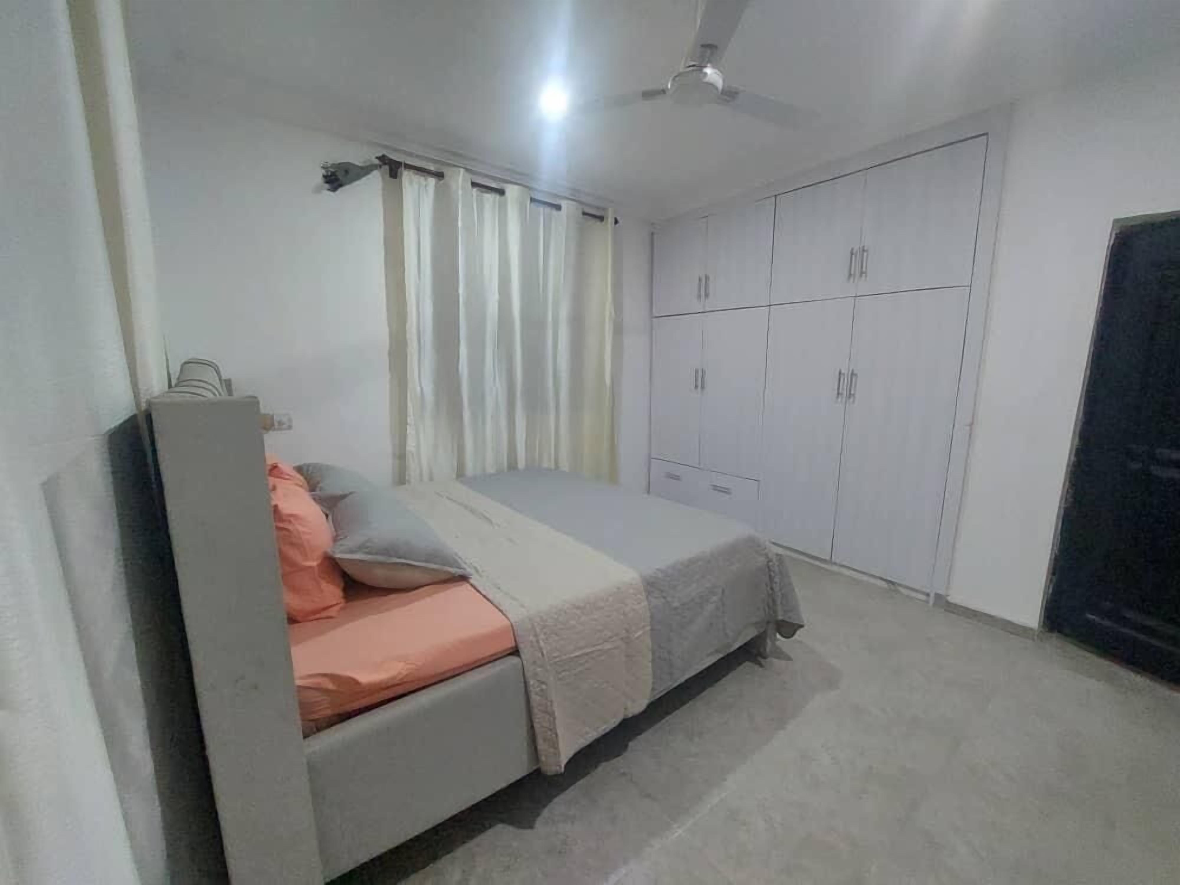 A bedroom with a bed, a wardrobe, a ceiling fan, and curtains.