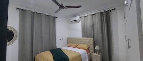 Un dormitorio con cama, cortinas, ventilador de techo y mesita de noche.