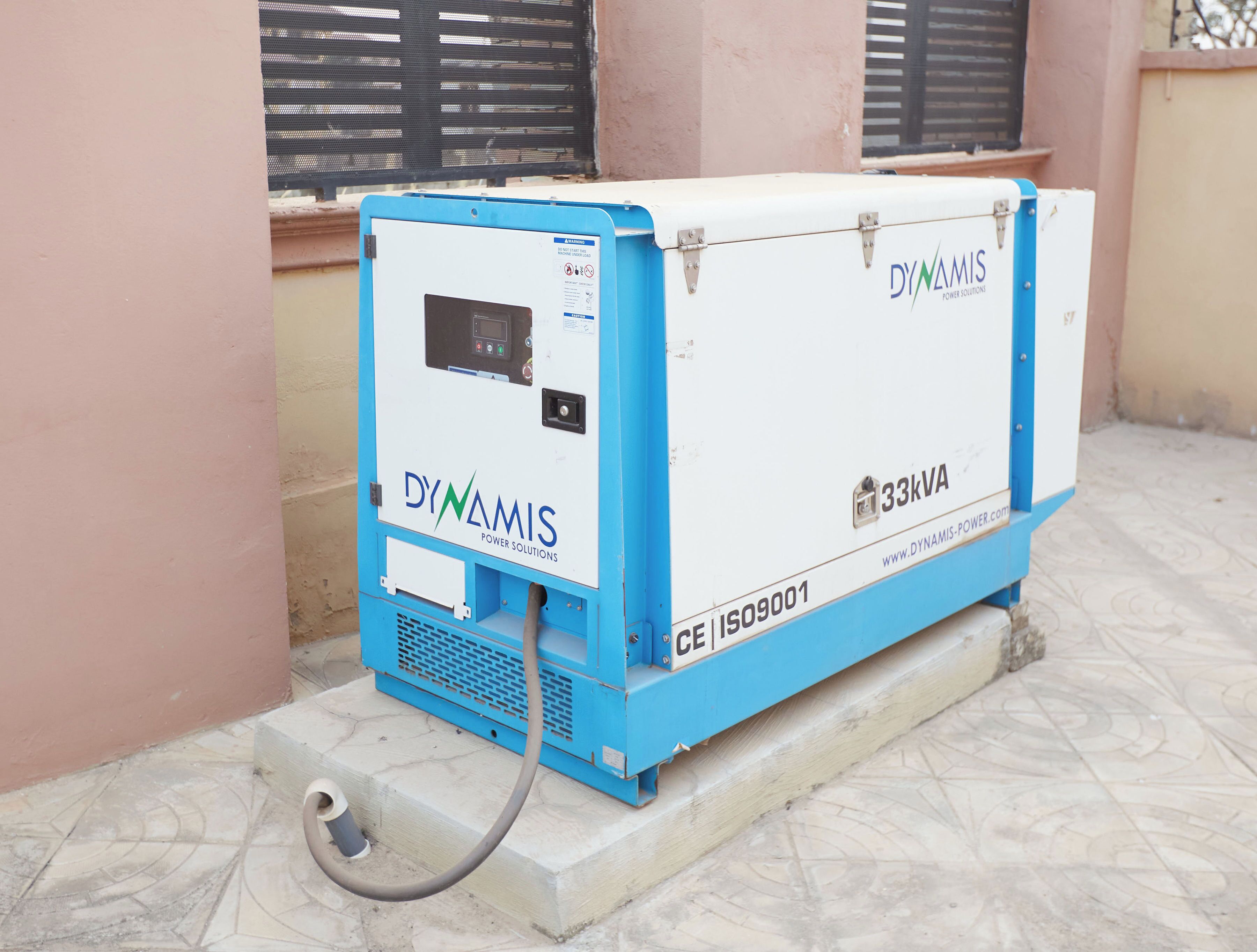Un generador portátil azul y blanco con la etiqueta 'DYNAMIS POWER SOLUTIONS', con una potencia de 33kVA, número de modelo CE 109001, y un panel de control visible.