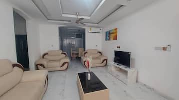 A modern living room with a sofa set, a coffee table, a flat-screen TV, and a ceiling fan.