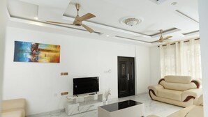 A modern living room with a flat-screen TV, a coffee table, and two sofas. - Monroe Luxury Apartments (Kumasi)