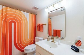 Une salle de bain avec un lavabo blanc, un miroir avec éclairage intégré, des toilettes et un rideau de douche à rayures orange.