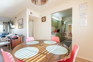 Un coin repas avec une table ronde en bois, des chaises roses et, au fond, une cuisine moderne.