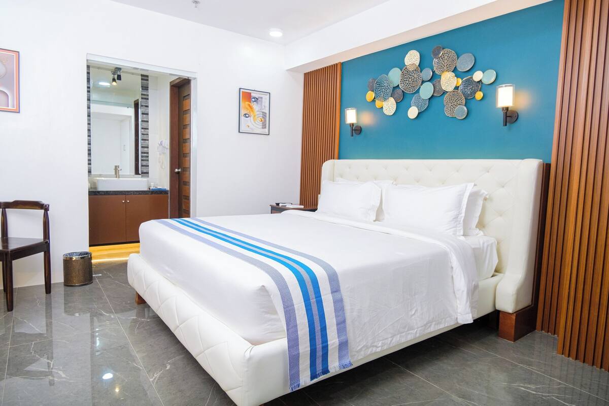 A hotel room with a large bed, a bathroom visible through an open door, and a decorative wall panel.