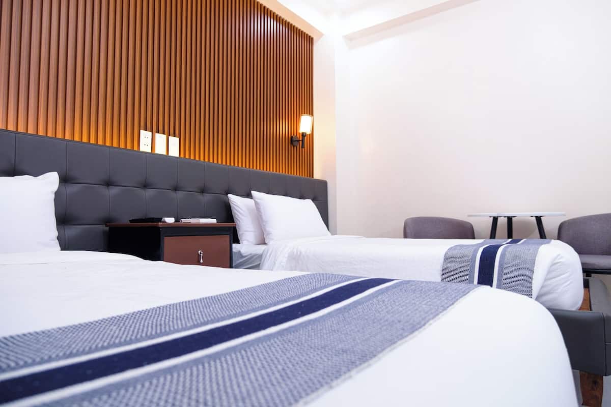 A hotel room with two beds, a wooden panel wall, a small table, and a chair.