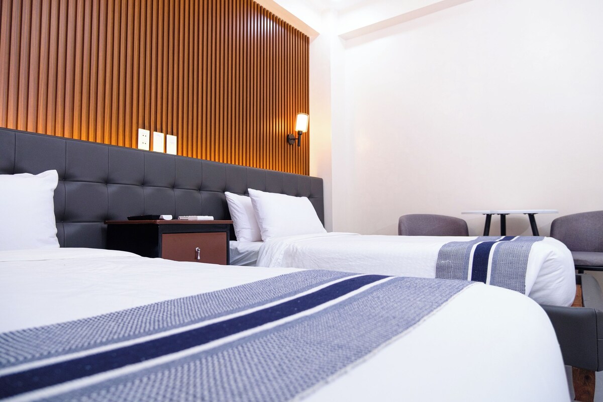 A hotel room with two beds, a wooden panel wall, a small table, and a chair.