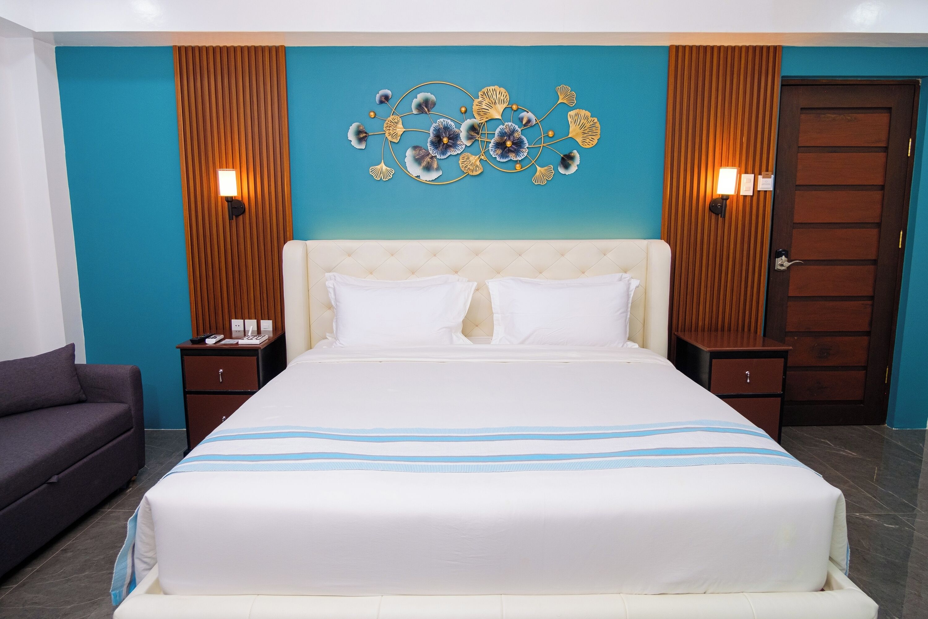Een hotelkamer met een groot bed, twee nachtkastjes, een bank en een decoratief wandobject.