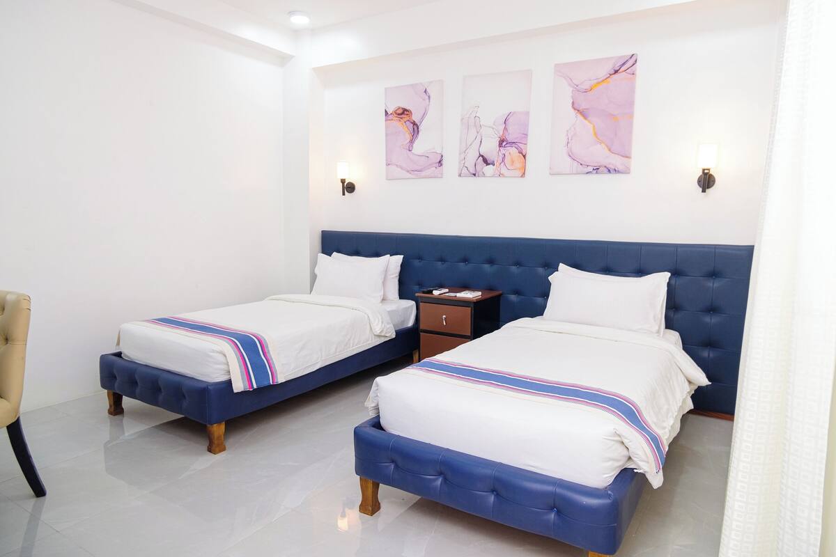 A hotel room with two beds, a nightstand, and a chair.