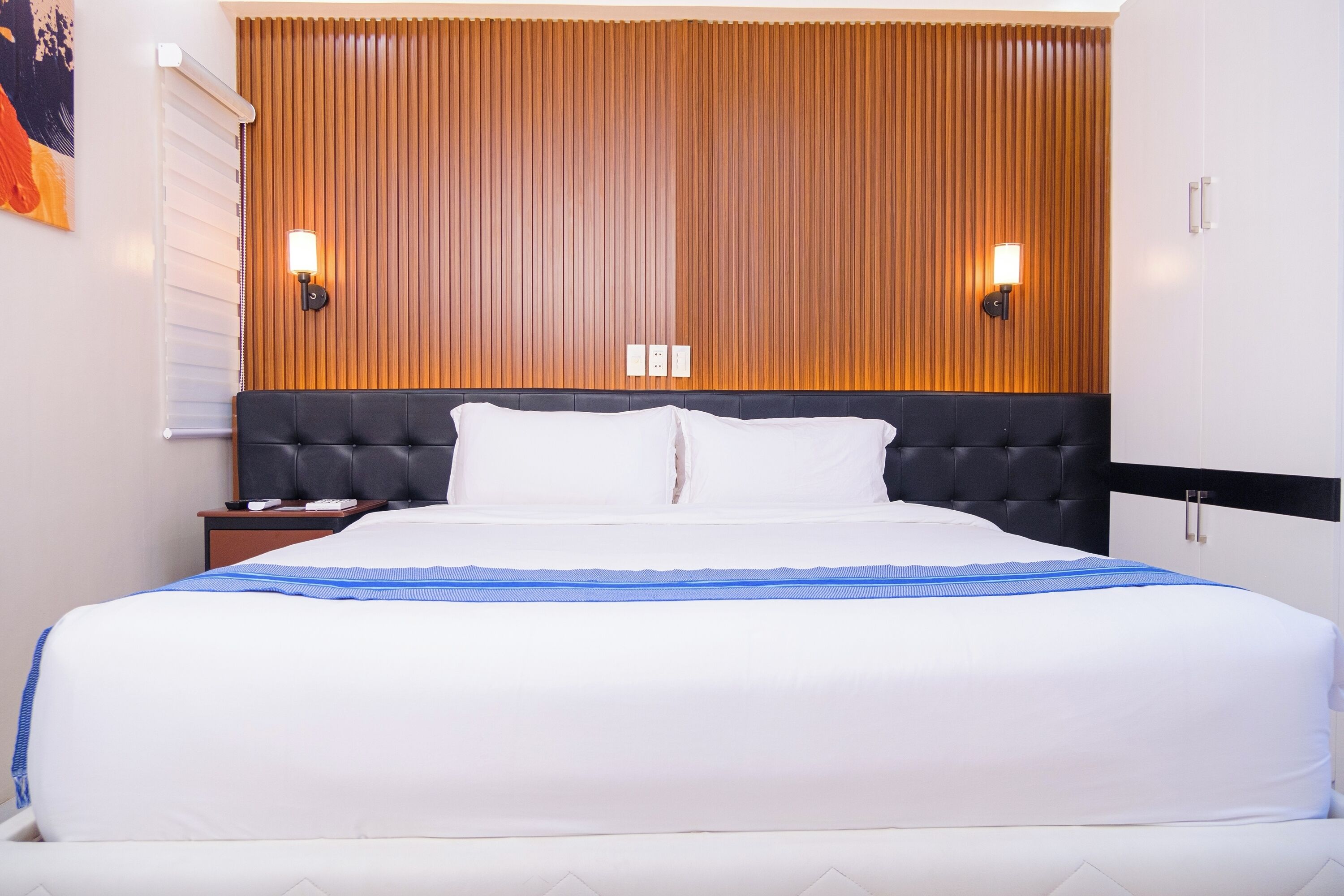 Ein Hotelzimmer mit einem großen Bett, einem Holzkopfteil, zwei Wandleuchten und einem Nachttisch mit einer Lampe.