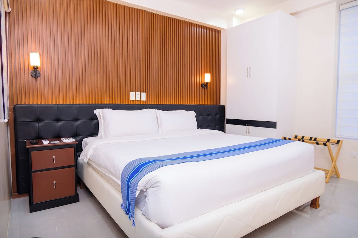 A modern bedroom with a large bed, wooden panel wall, bedside lamps, and a wardrobe.