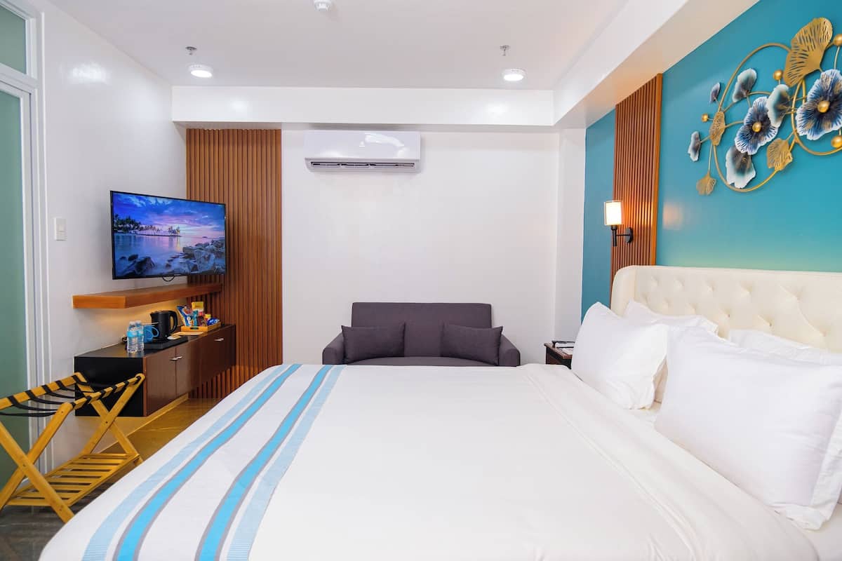 A hotel room with a large bed, a TV, a desk with a chair, and a decorative wall piece.