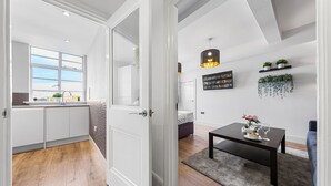 A modern kitchen with white cabinets, a large window, and a wooden floor. - 1 Bed Flat - Sleeps 4 - Parking - Wifi (Central London)