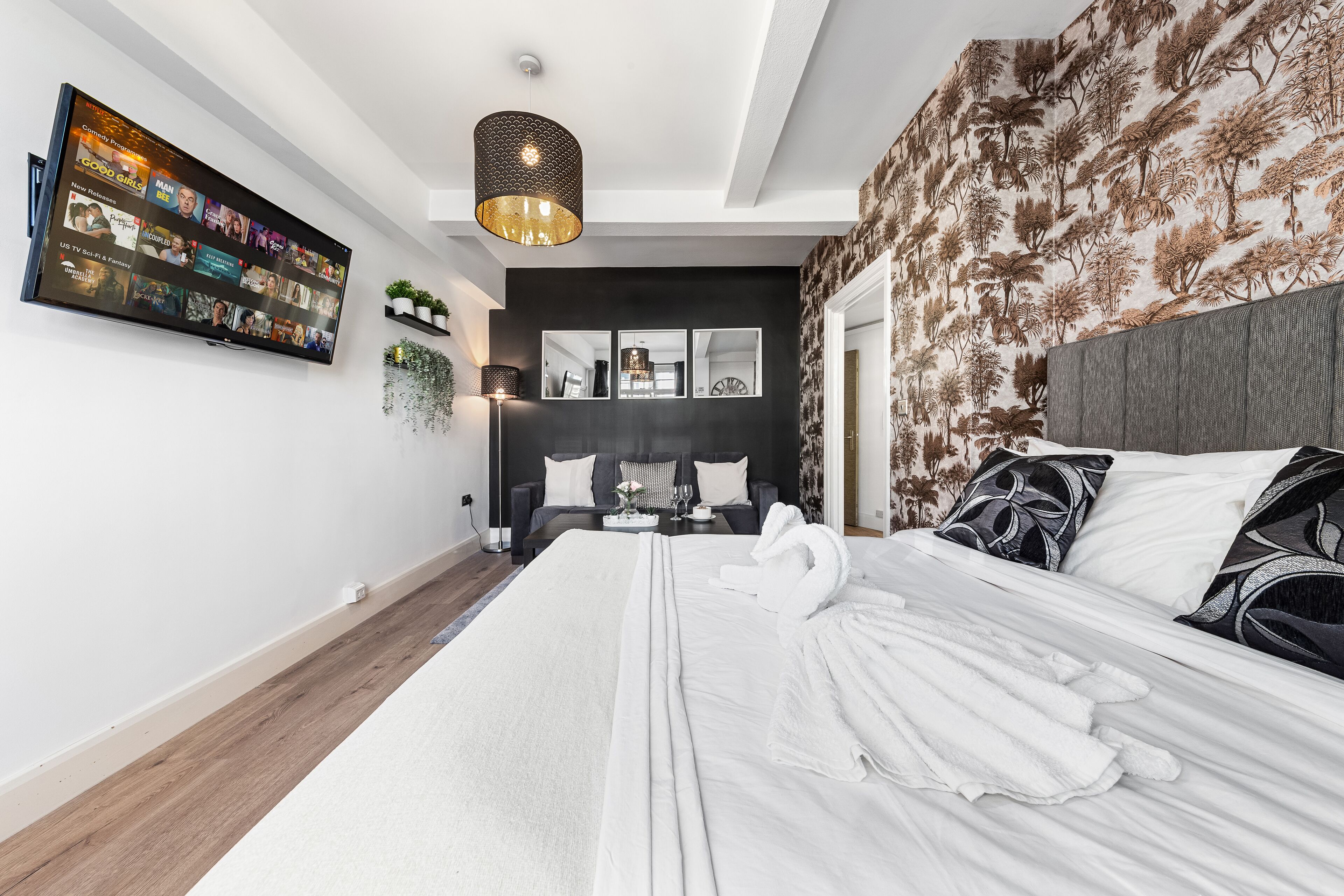A modern hotel room with a large bed, a flat-screen TV mounted on the wall, a unique patterned wallpaper, and a stylish pendant light.