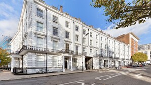 A multi-story building with a white facade, large windows, and a black wrought iron balcony. - 1 Bed Flat - Sleeps 4 - Parking - Wifi (Central London)