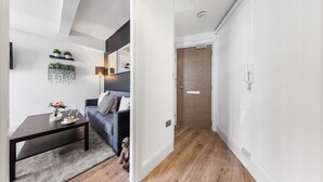 A modern living room with a dark wooden coffee table, a grey sofa, and a small rug. There are potted plants on the wall and a lamp on the side table. - 1 Bed Flat - Sleeps 4 - Parking - Wifi (Central London)