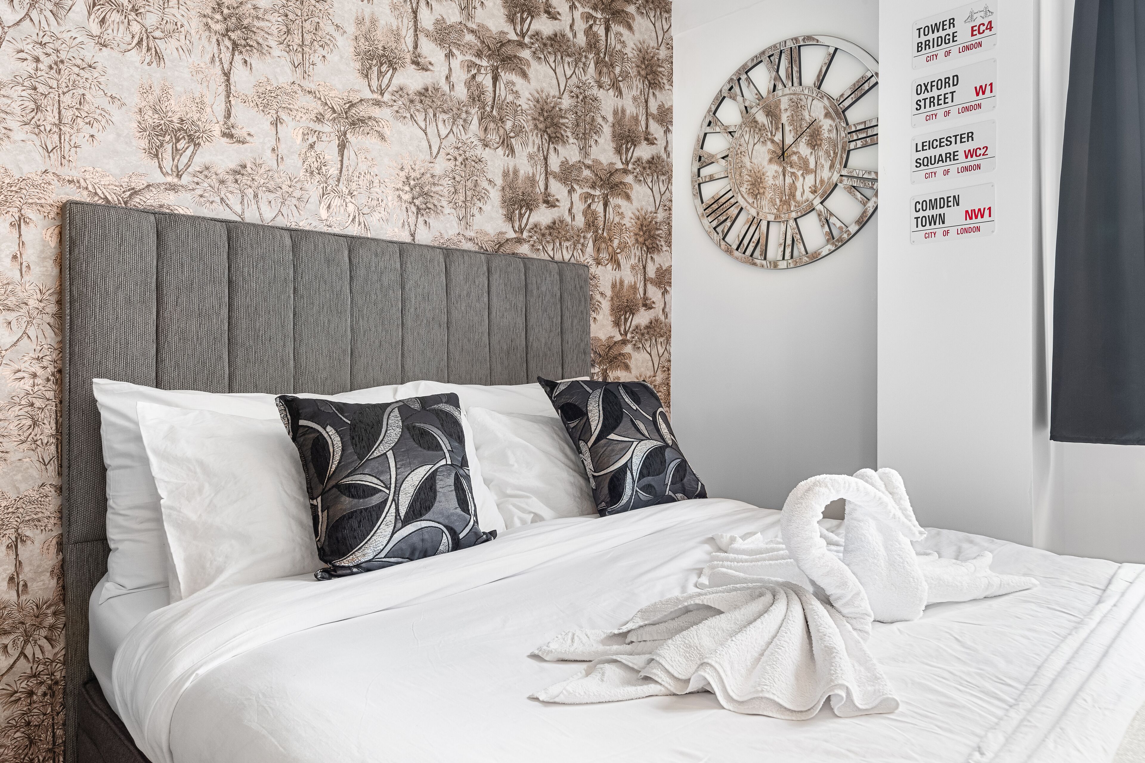 Een net opgemaakt bed met witte beddengoed en een witte badjas, een grijs hoofdeinde en een wandklok.