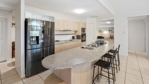 A modern kitchen with a stainless steel refrigerator, granite countertop, and bar stools.