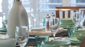 A dining table set with green plates, clear glasses, and a white vase with dried flowers.