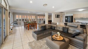 A modern living room with a sectional sofa, a dining area with a table and chairs, and a kitchen with stainless steel appliances.