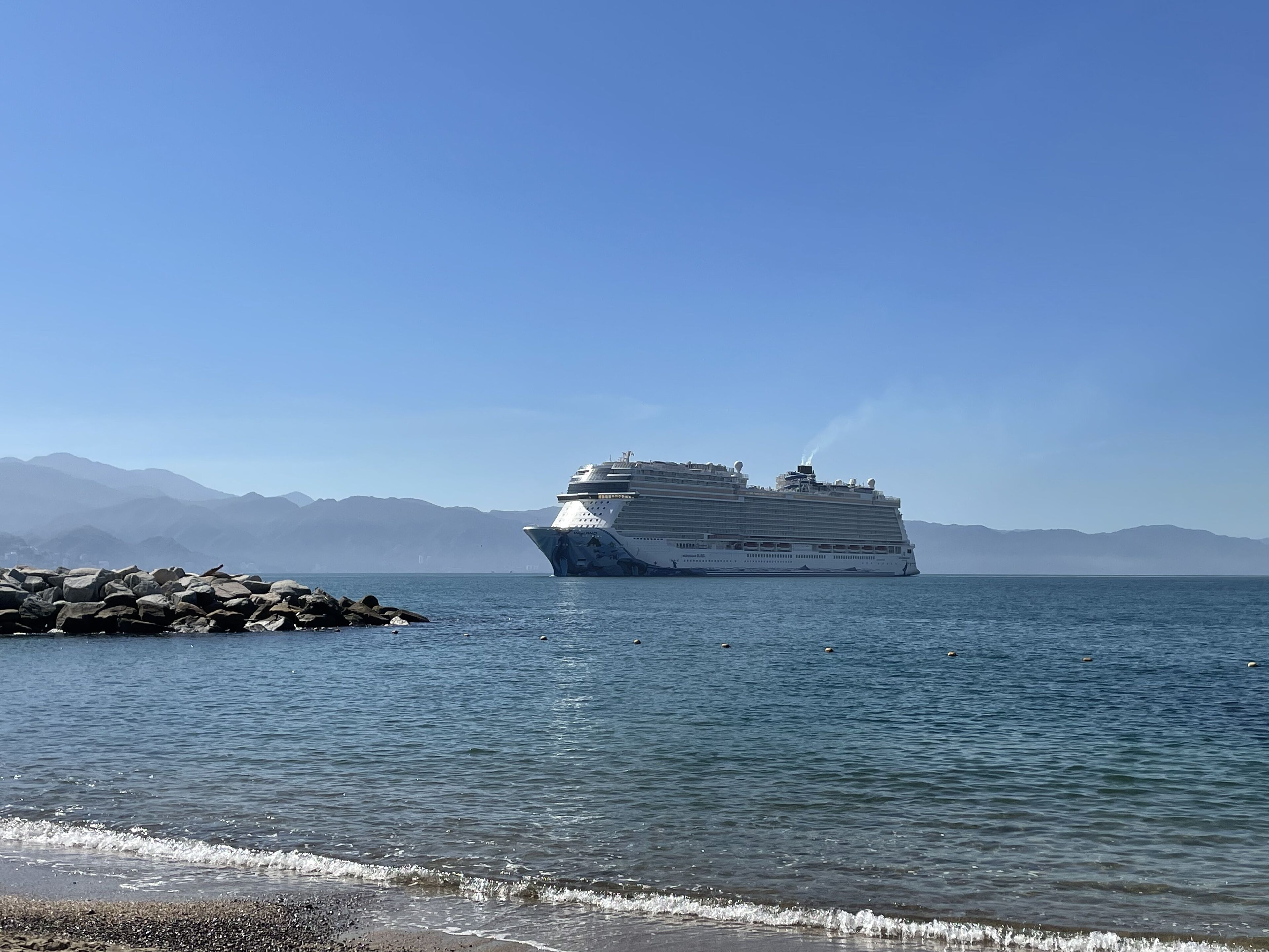 Un grand navire de croisière était amarré à un quai rocheux, avec des montagnes en toile de fond.