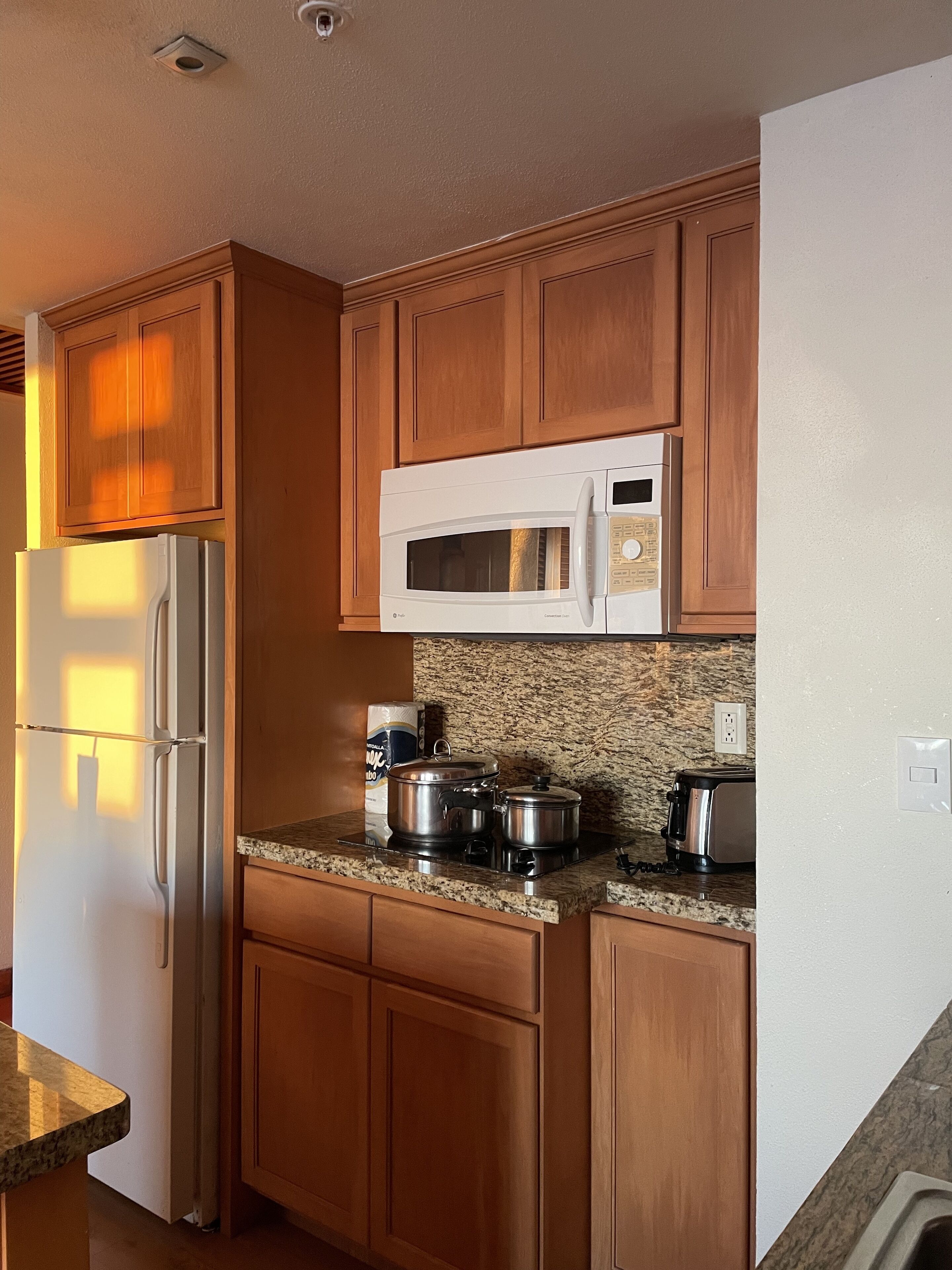 A kitchen with wooden cabinets, a stainless steel refrigerator, a microwave, a stove, and a toaster.