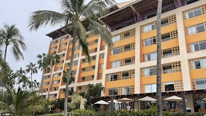 Ein mehrstöckiges Hotel mit Balkonen, Palmen und Außenbereich-Sitzgelegenheiten.