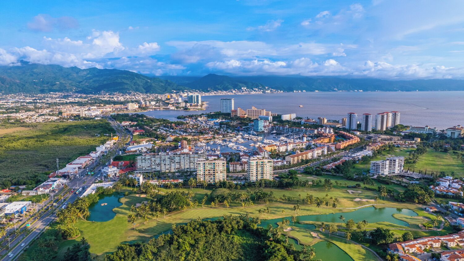 A coastal cityscape with a marina, high-rise hotels, and a golf course.