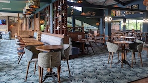 Ein Restaurant mit modernem Interieur, das eine Mischung aus Holz- und Polstersitzgelegenheiten, einem gemusterten Boden und verschiedenen Hängelampen bietet.
