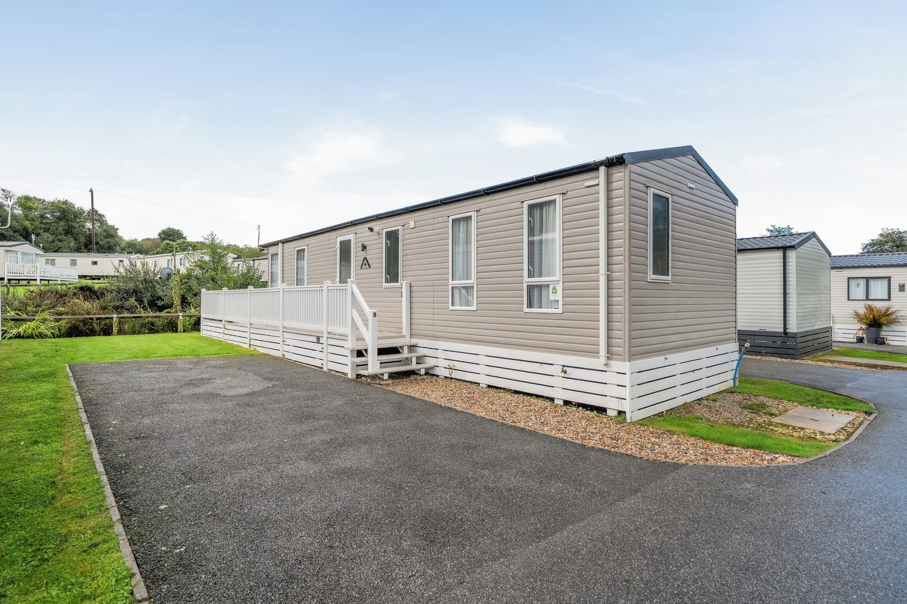 A single-story mobile home with a front porch and a gravel driveway.