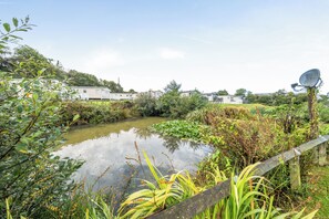 A serene outdoor setting with a pond, lush greenery, and mobile homes in the background.