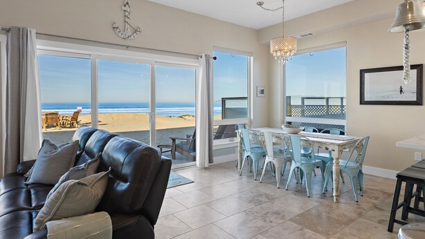 A spacious living area with a leather couch, a dining table with chairs, and large sliding glass doors leading to a beach view.