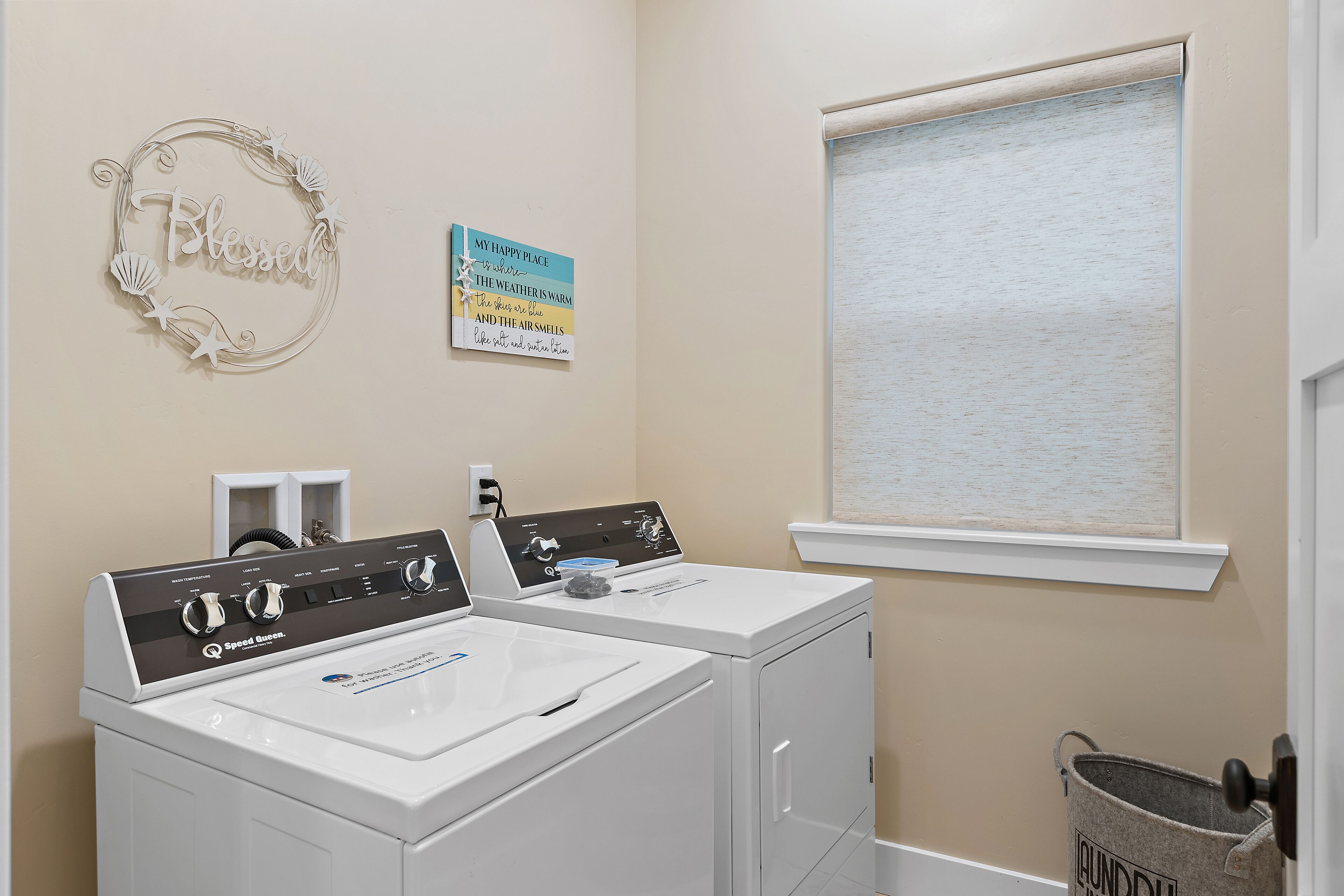 A laundry room with two front-loading washing machines, a wall-mounted dryer, and a window with blinds.