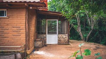A rustic cabin with a brick exterior, a wooden porch, and a dirt ground.