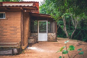 A rustic cabin with a brick exterior, a wooden porch, and a dirt ground. - Cabaña Tabachín - Su conexión con la naturaleza (Huatulco)