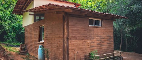 Une petite maison en briques, avec un toit en tuiles, entourée de verdure.
